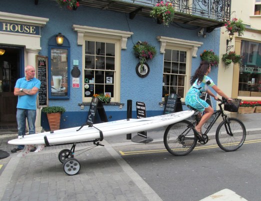 Woman Pulling Surfboard On A Bicycle